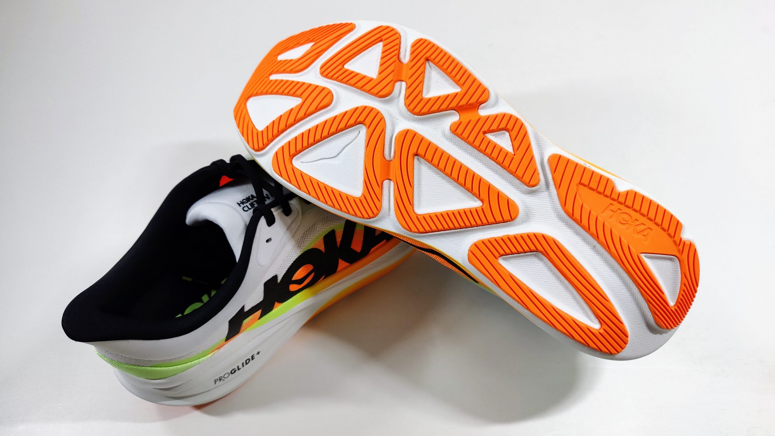Underside of a running shoe with orange rubber outsole pods and triangular white foam cutouts, placed on a white surface.