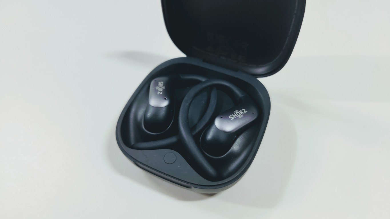 Open charging case with two black open-ear earbuds with ear hooks inside