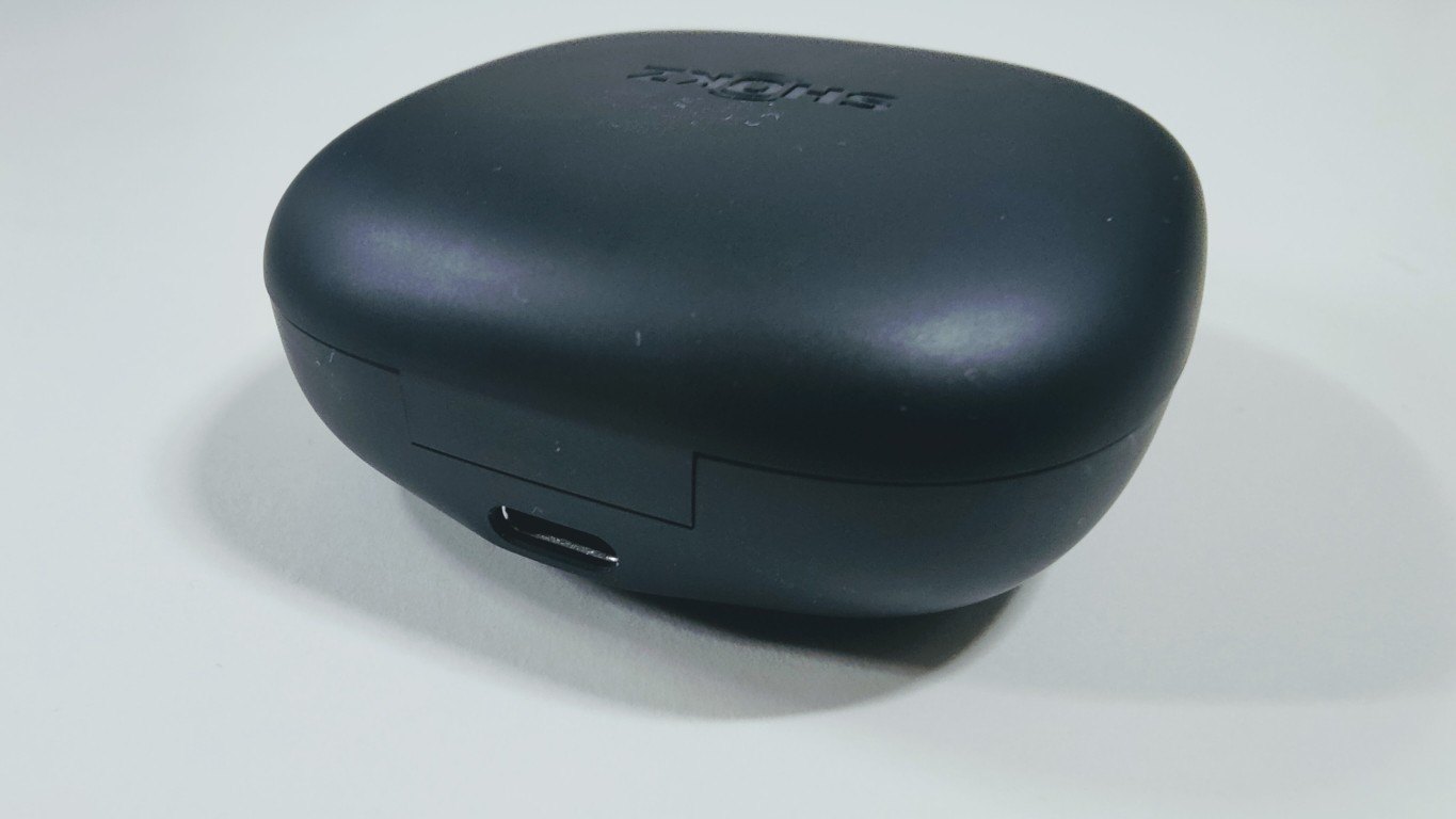 Side view of the charging case showing the USB-C port, placed on a white surface